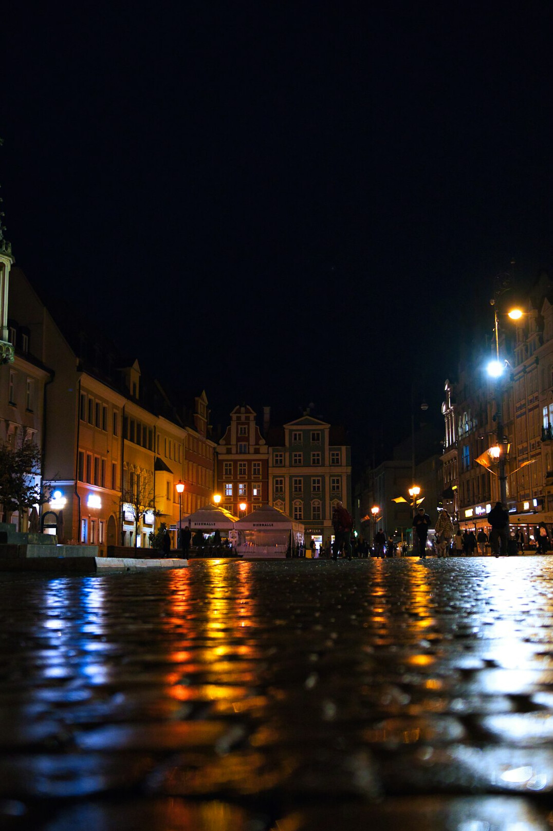 Rainy cobblestone street at night in an old city with warm street lamps